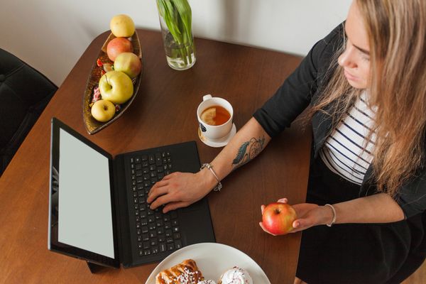 אישה מחזיקה תפוח ומסתכלת במחשב הנייד