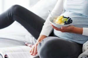 אישה בהריון אוכלת קערת יוגורט עם פירות